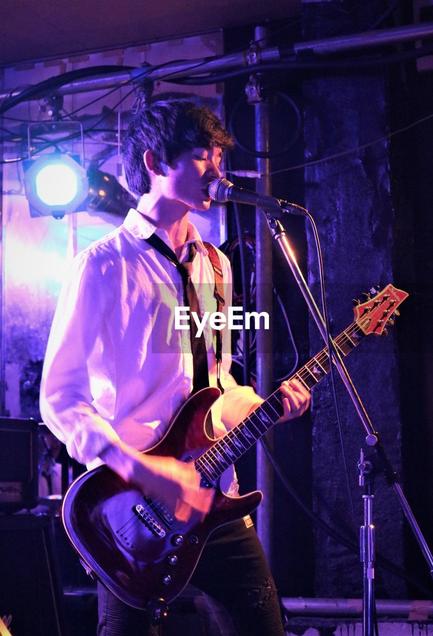 Teenage boy playing guitar at music concert