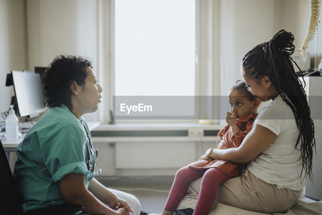 Woman carrying ill daughter discussing with pediatric in clinic