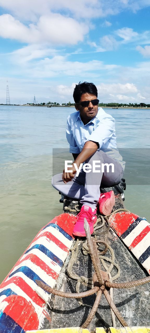 water, one person, boating, nautical vessel, vehicle, nature, sea, transportation, boat, men, adult, full length, day, sky, cloud, sitting, young adult, leisure activity, outdoors, casual clothing, mode of transportation, lifestyles, watercraft, looking at camera, portrait, beach, holiday, vacation, smiling, emotion, person, life jacket, trip, travel, land