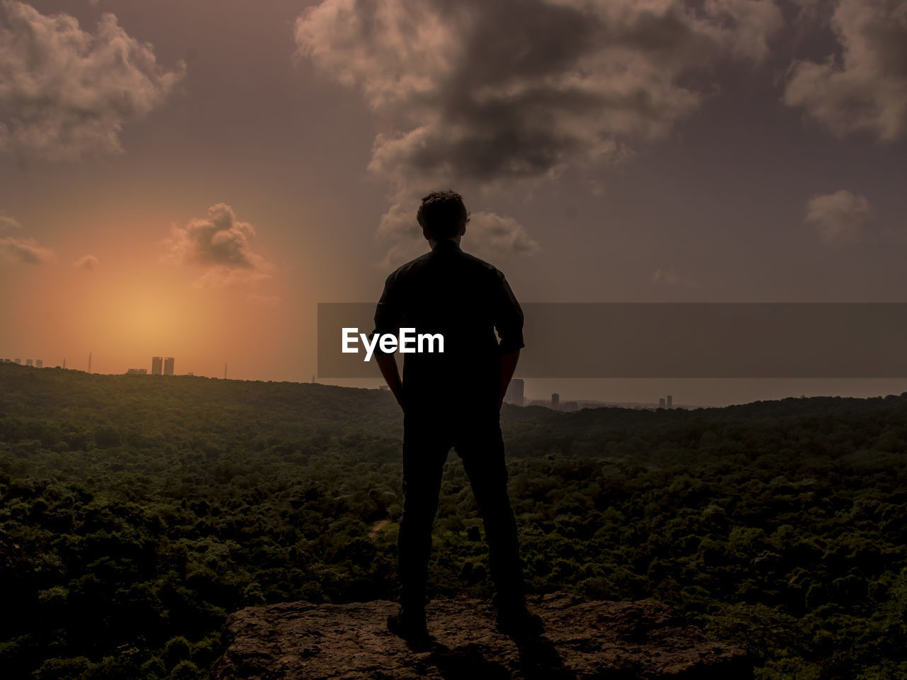 Rear view of man standing on field against sky during sunset
