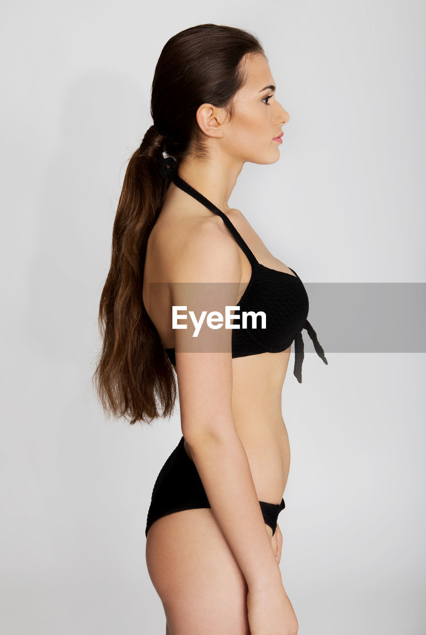 Side view of teenage girl wearing black lingerie standing against white background