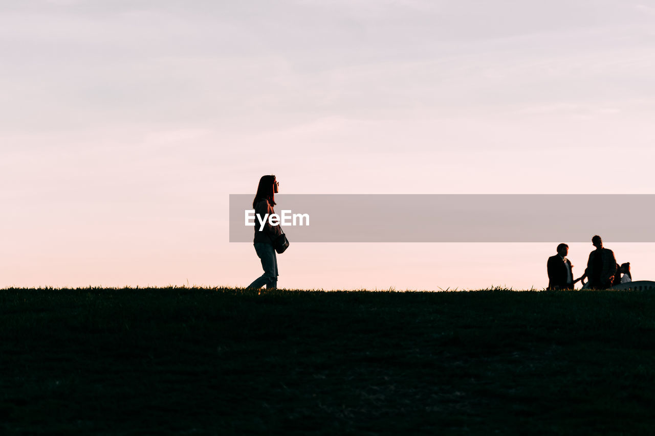 Woman walking on land against sky during sunset