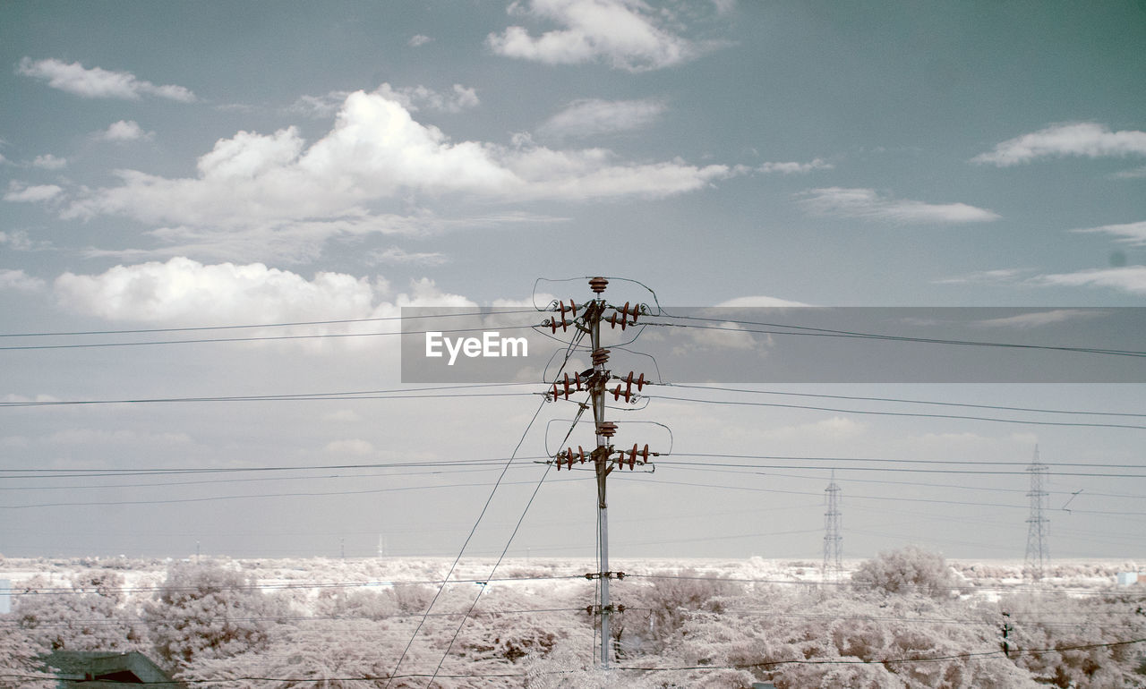 Electricity pylon on snow covered field against sky