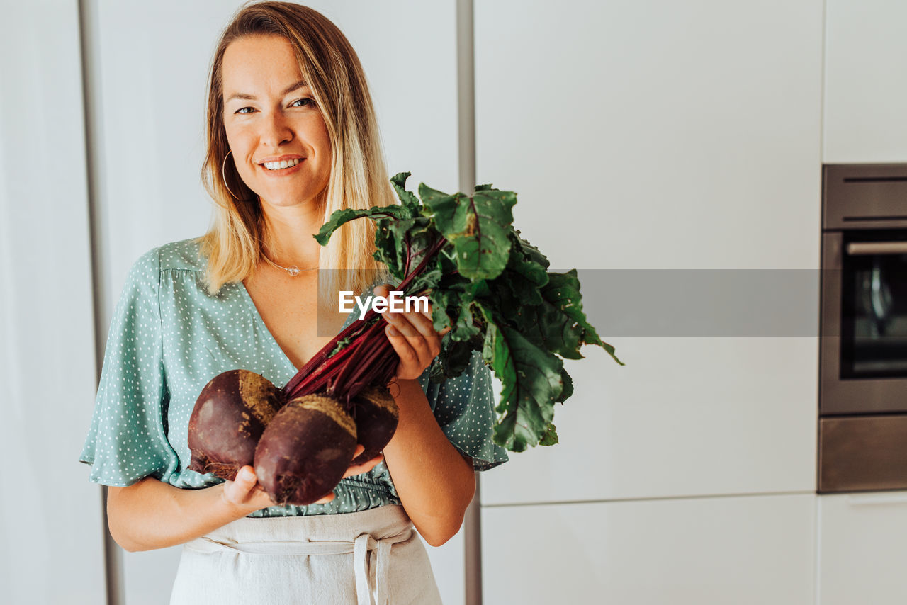 Young european woman holding beetroot while smiling at camera