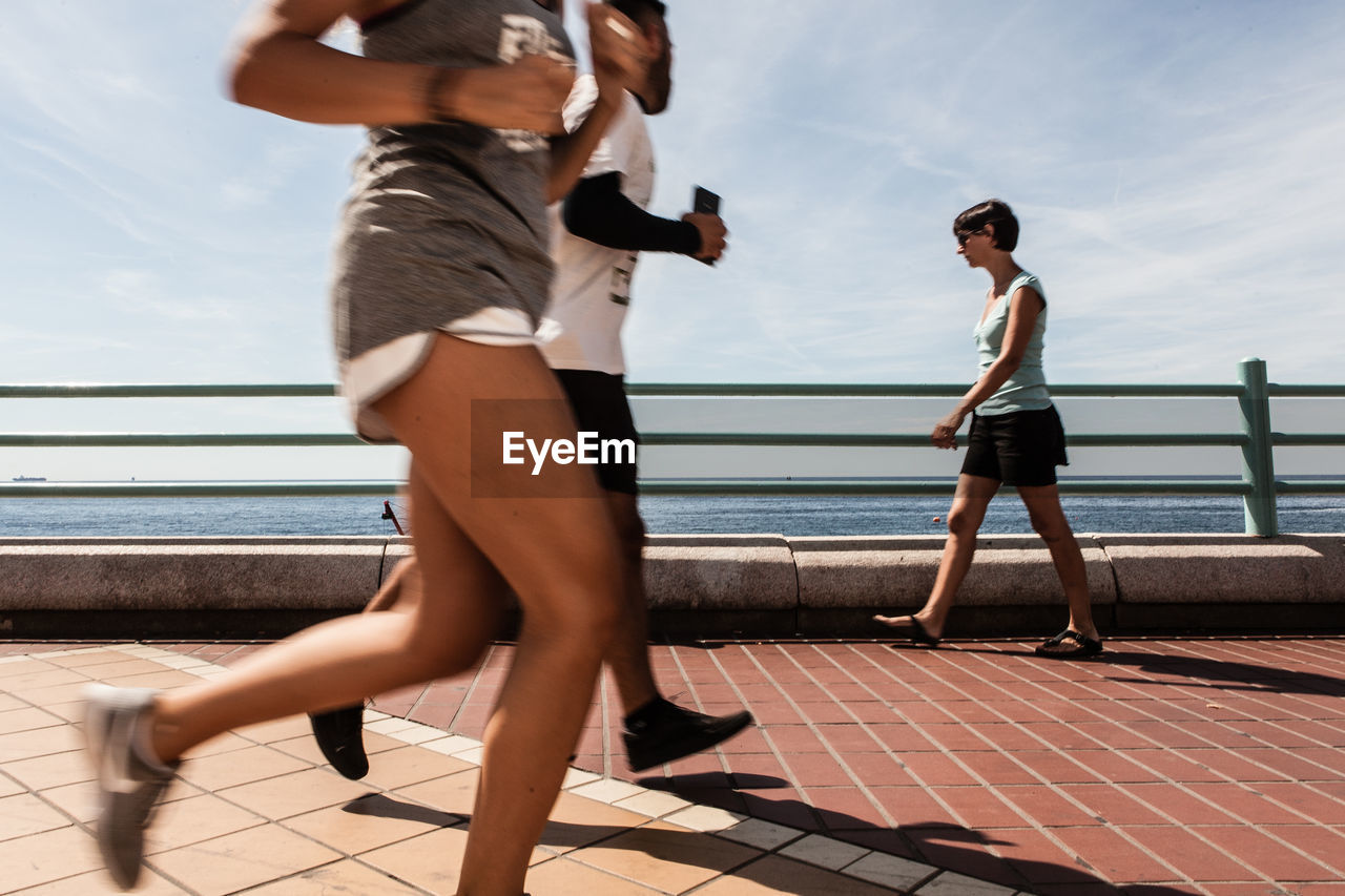 Athlete jogging on promenade by sea against sky