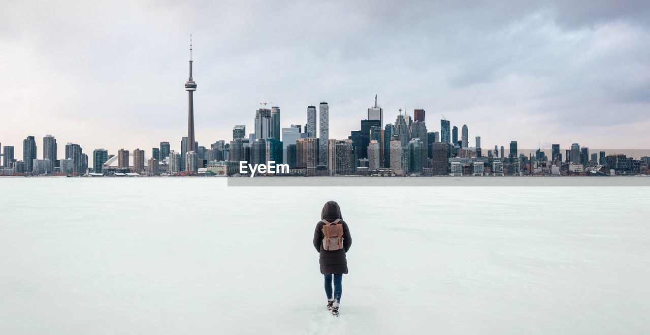 Rear view of woman walking on frozen lake ontario with financial district in background