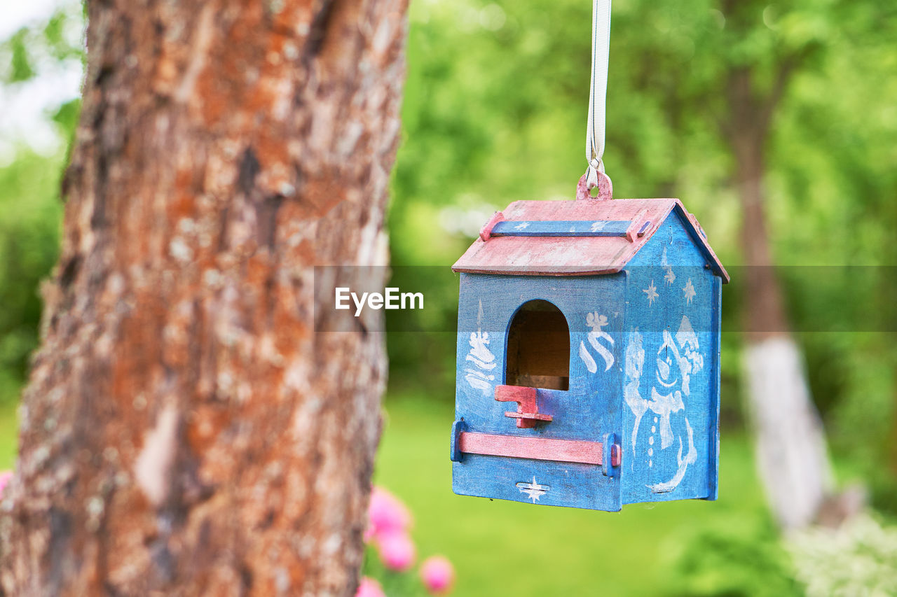 CLOSE-UP OF BIRDHOUSE ON WOODEN POST AGAINST TREE TRUNK