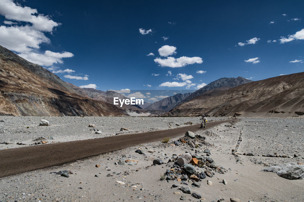 Path amidst landscape and mountains against cloudy sky