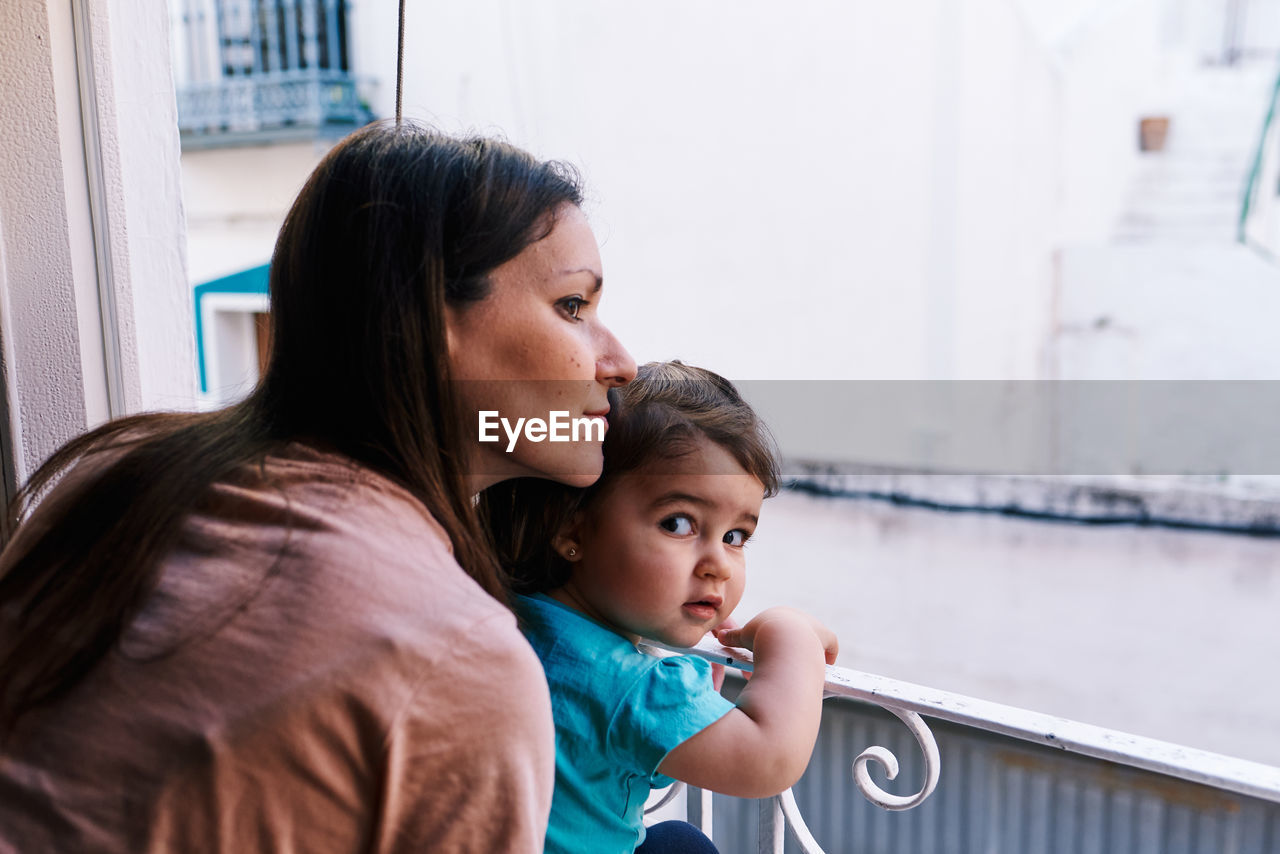 Mother and daughter looking out the window of the house happy