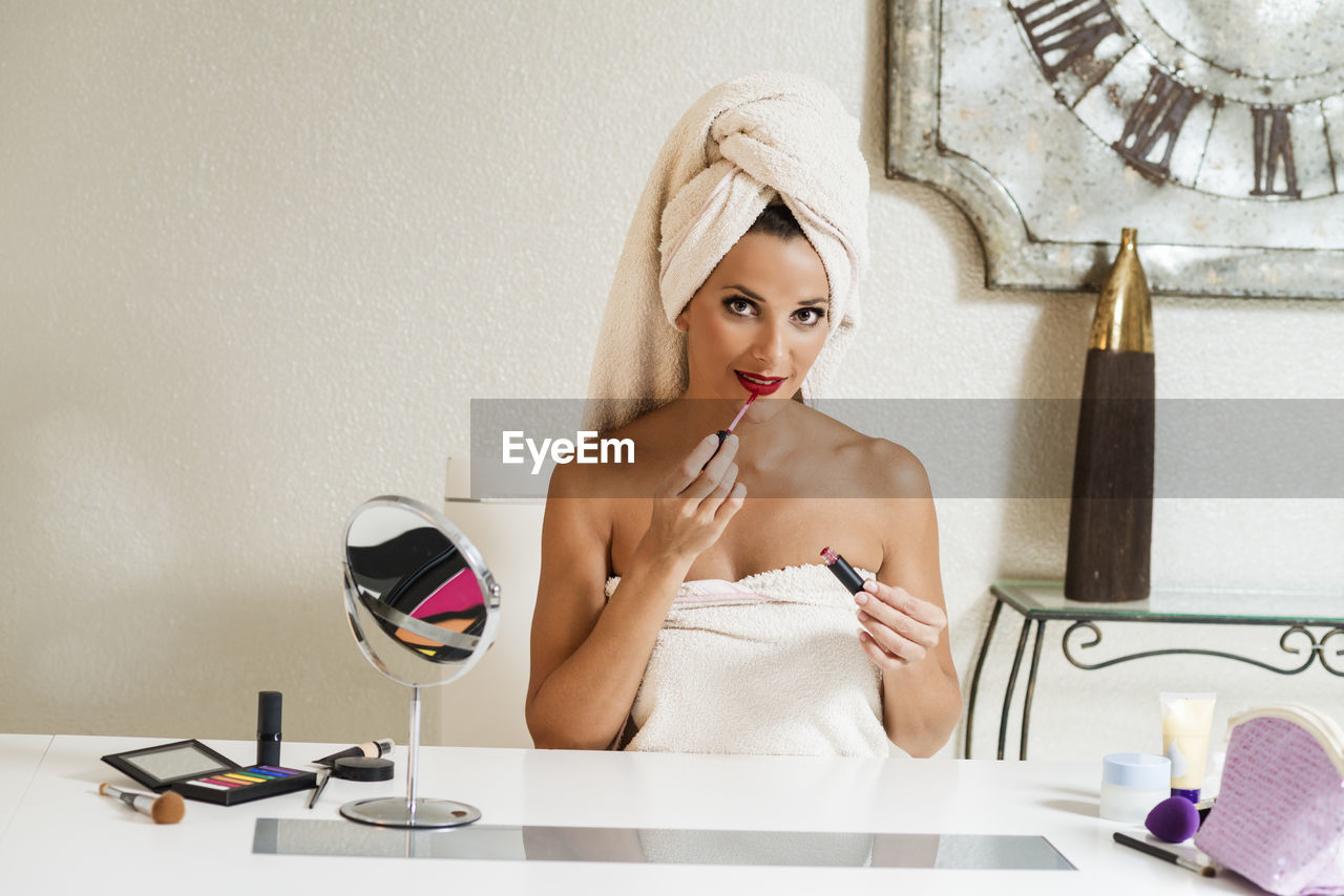 PORTRAIT OF YOUNG WOMAN AGAINST WALL IN BATHROOM