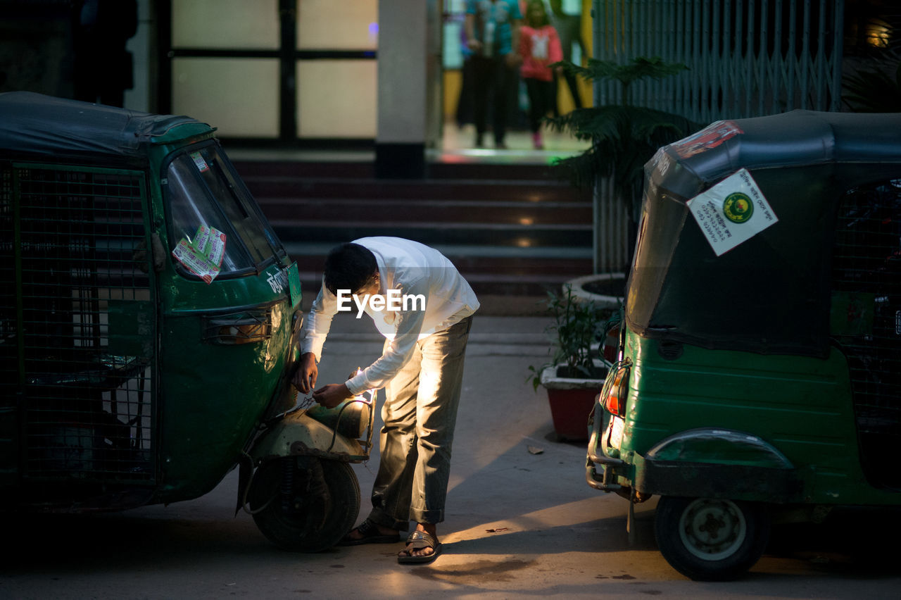 Man bending over jinricksha on street against building