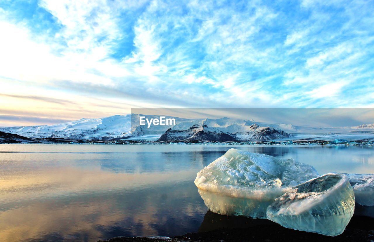 Scenic view of snowcapped mountains by lagoon against cloudy sky