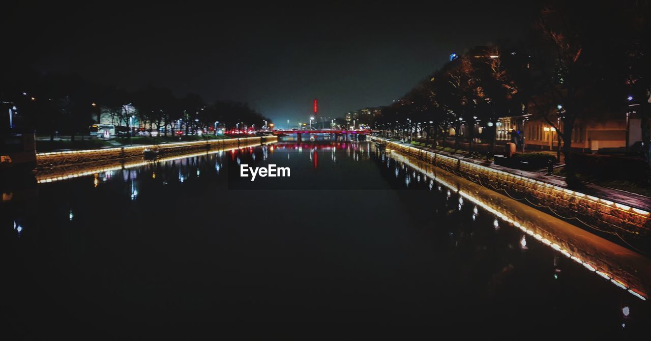 Illuminated bridge over river by buildings in city at night