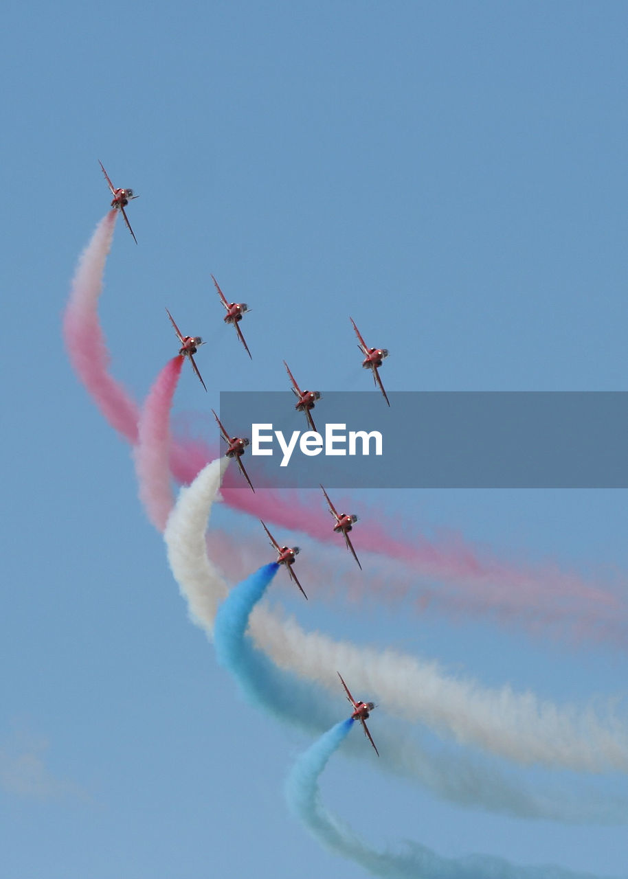 LOW ANGLE VIEW OF AIRSHOW IN FLIGHT AGAINST BLUE SKY