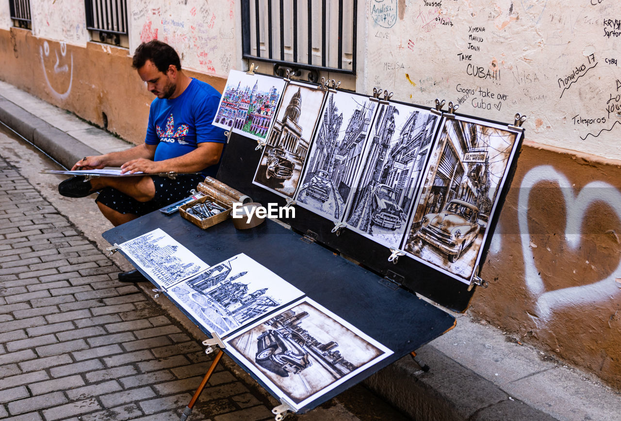 HIGH ANGLE VIEW OF MAN USING PHONE WHILE SITTING IN CITY