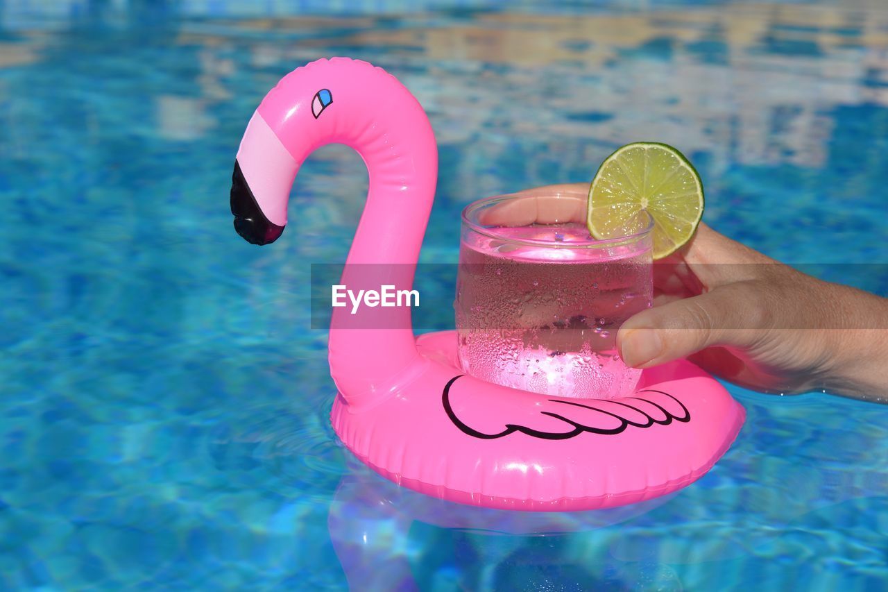 Cropped hand holding drink on inflatable ring in swimming pool