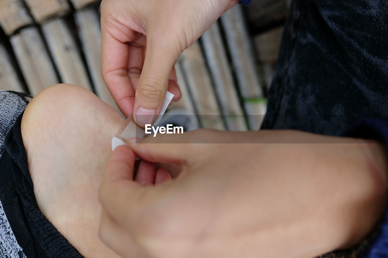 Cropped hands of person applying adhesive bandage on ankle