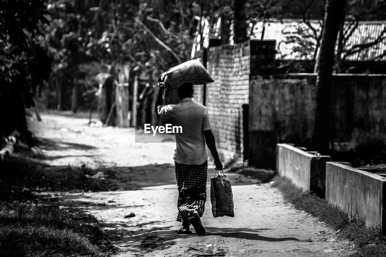 Rear view of man carrying sack while walking on road