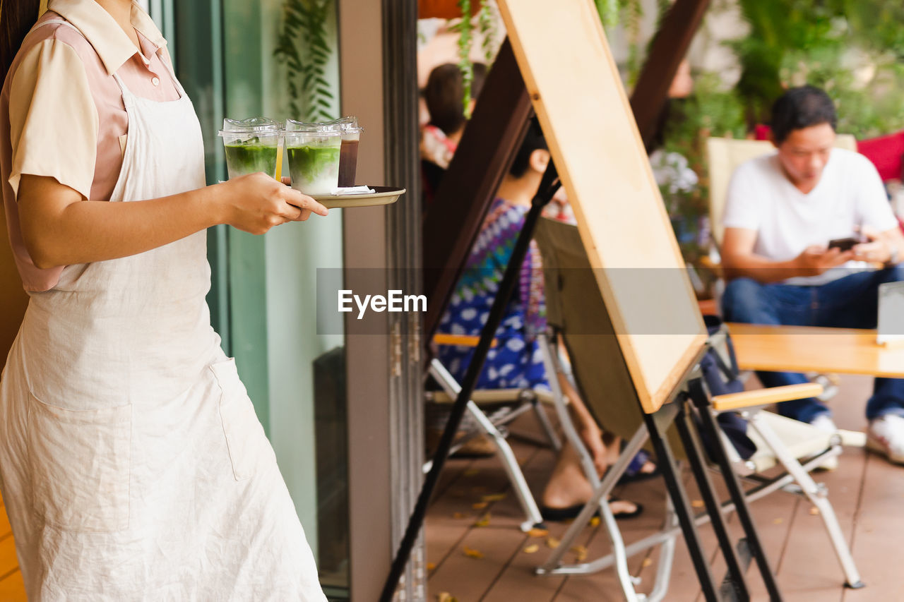 Waitress with apron serving iced matcha latte to customer at cafe.