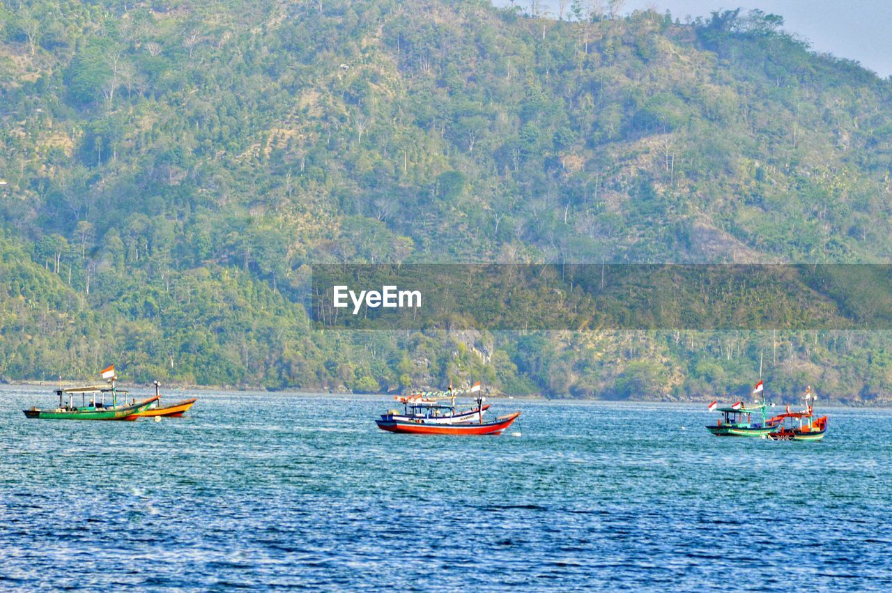 Boats sailing in sea against mountains