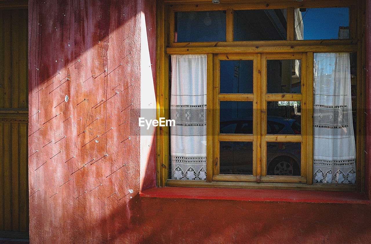 Closed window in sun rays showing laced curtains on a red building 