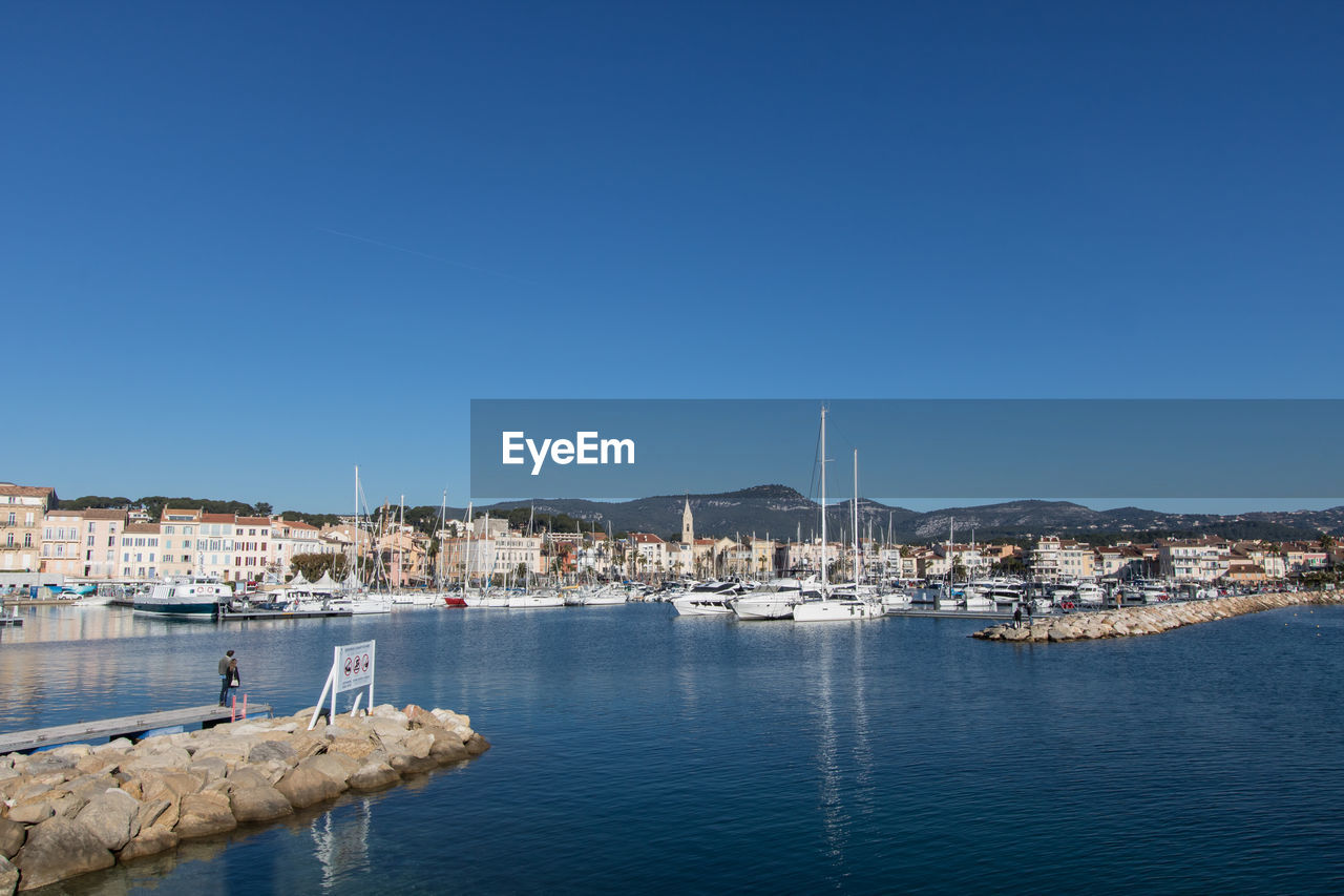 Sailboats in sea by buildings against clear blue sky