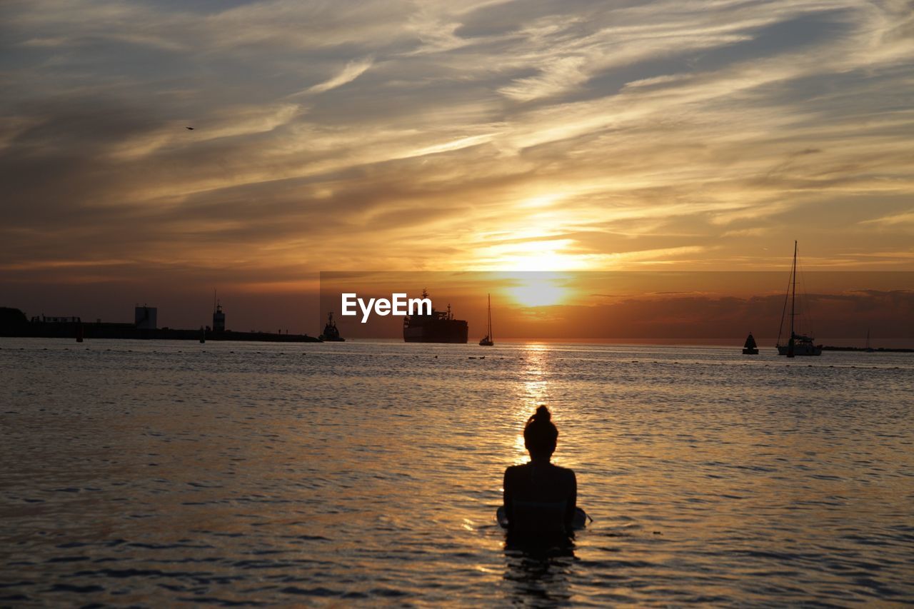 Rear view of woman in sea against sky during sunset