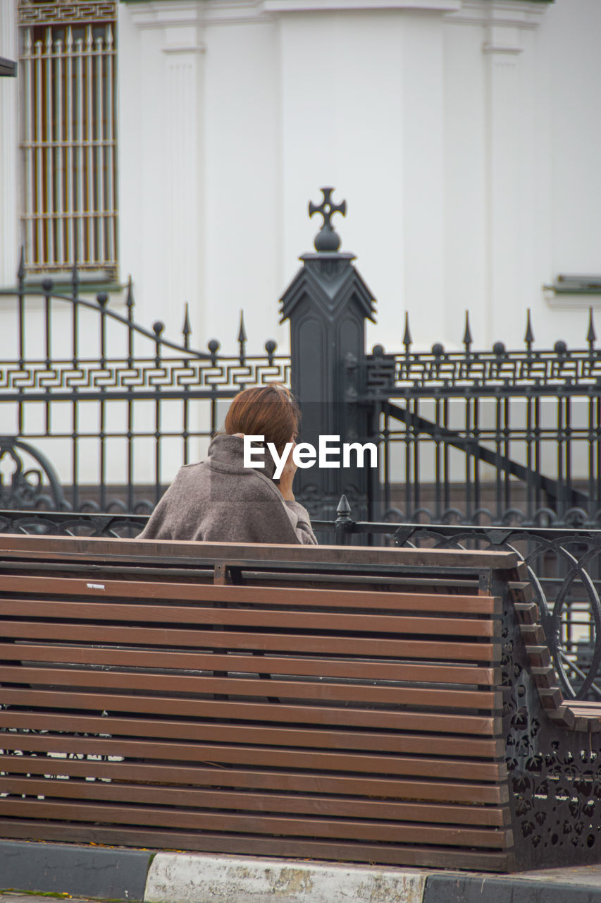 Rear view of man sitting on railing against building