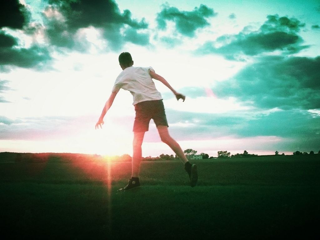 Full length rear view of man on grassy field against sky during sunset