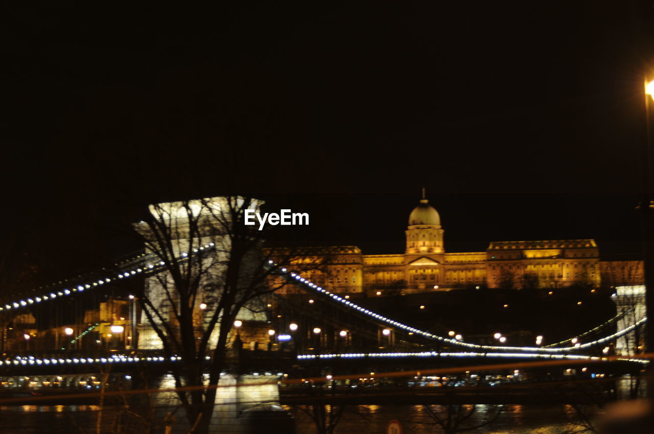 VIEW OF ILLUMINATED BRIDGE OVER RIVER AT NIGHT