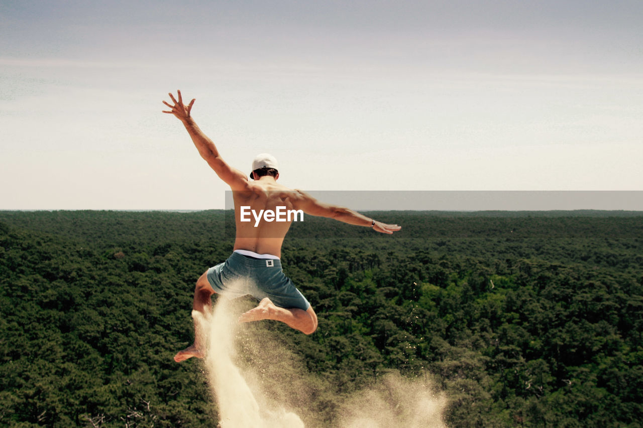 Full length of shirtless man jumping over landscape against sky