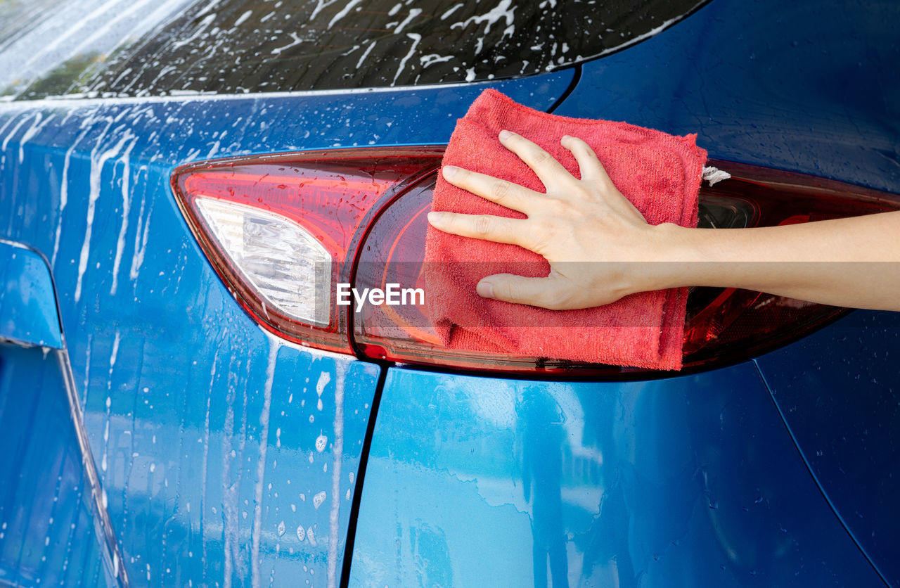 Car wash service. car covered with white soap foam. man hand holding red microfiber cloth and polish