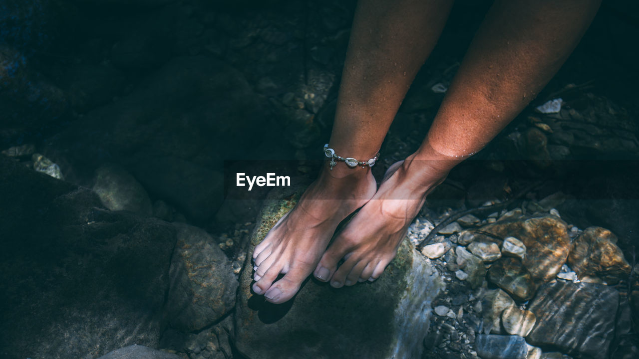 Low section of woman wearing jewelry on rock in lake