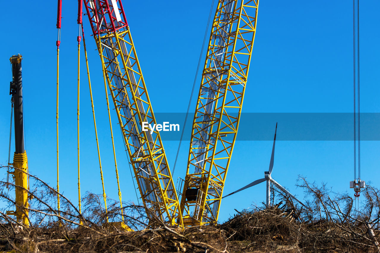 LOW ANGLE VIEW OF CRANES AGAINST BLUE SKY