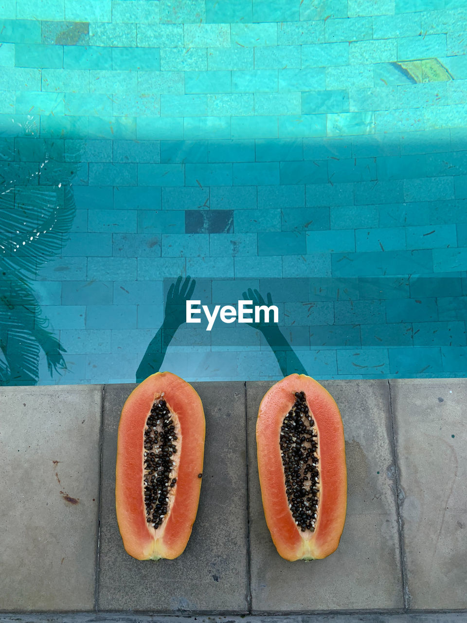 Shadows of hands on the water in the pool and cut papaya