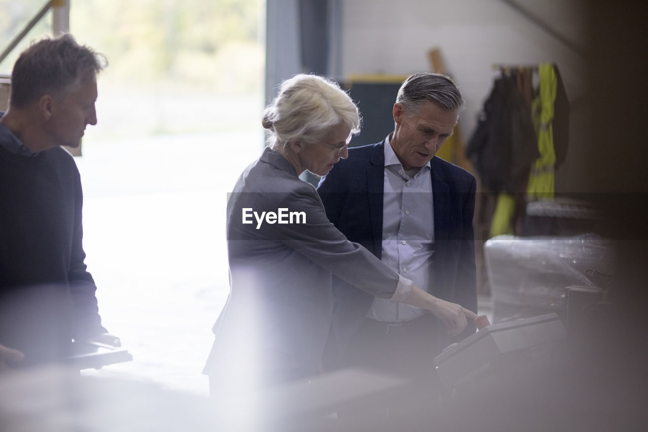 Business people operating machine while standing at industry