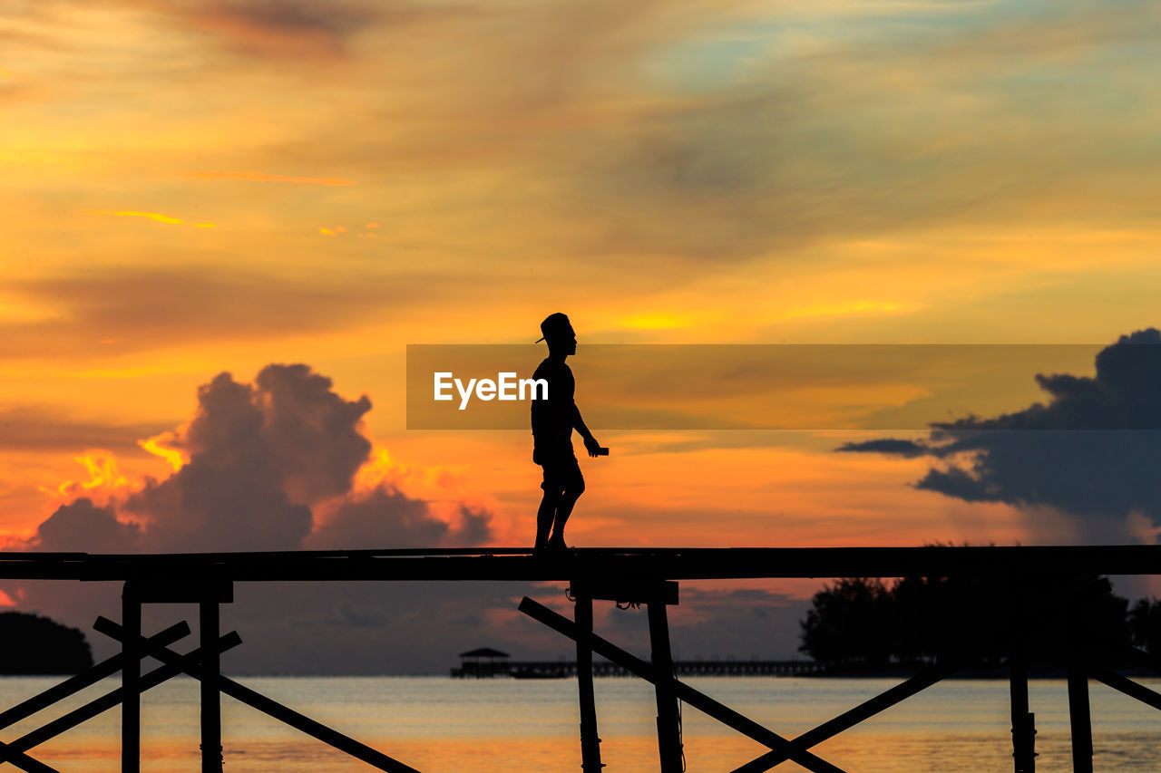 Silhouette man walking on pier over sea against sky during sunset