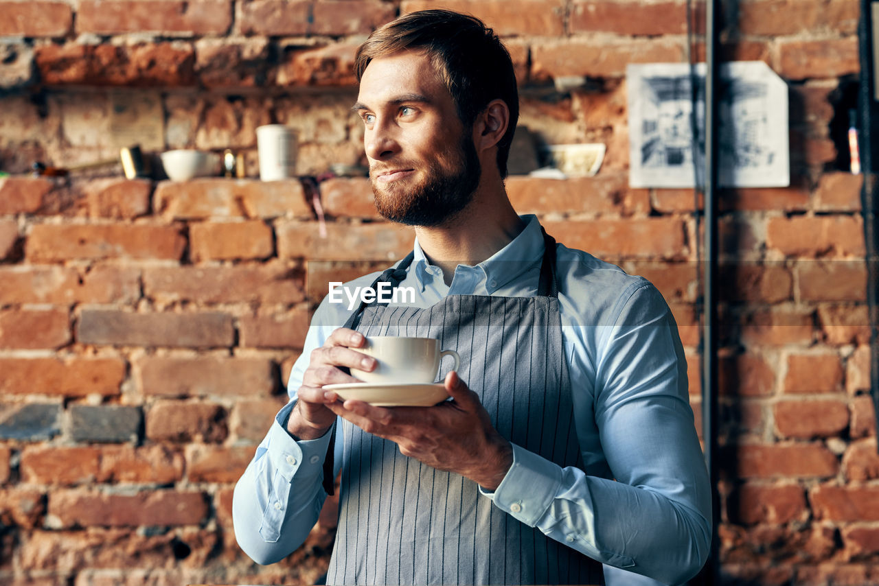 Portrait of young man with coffee cup against wall