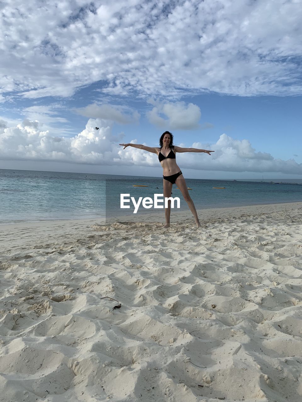 Full length of woman wearing bikini while standing at beach against sky
