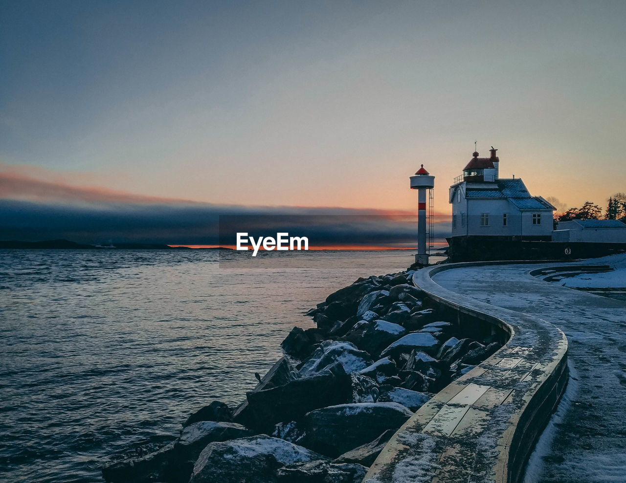 Lighthouse by sea against sky during sunset