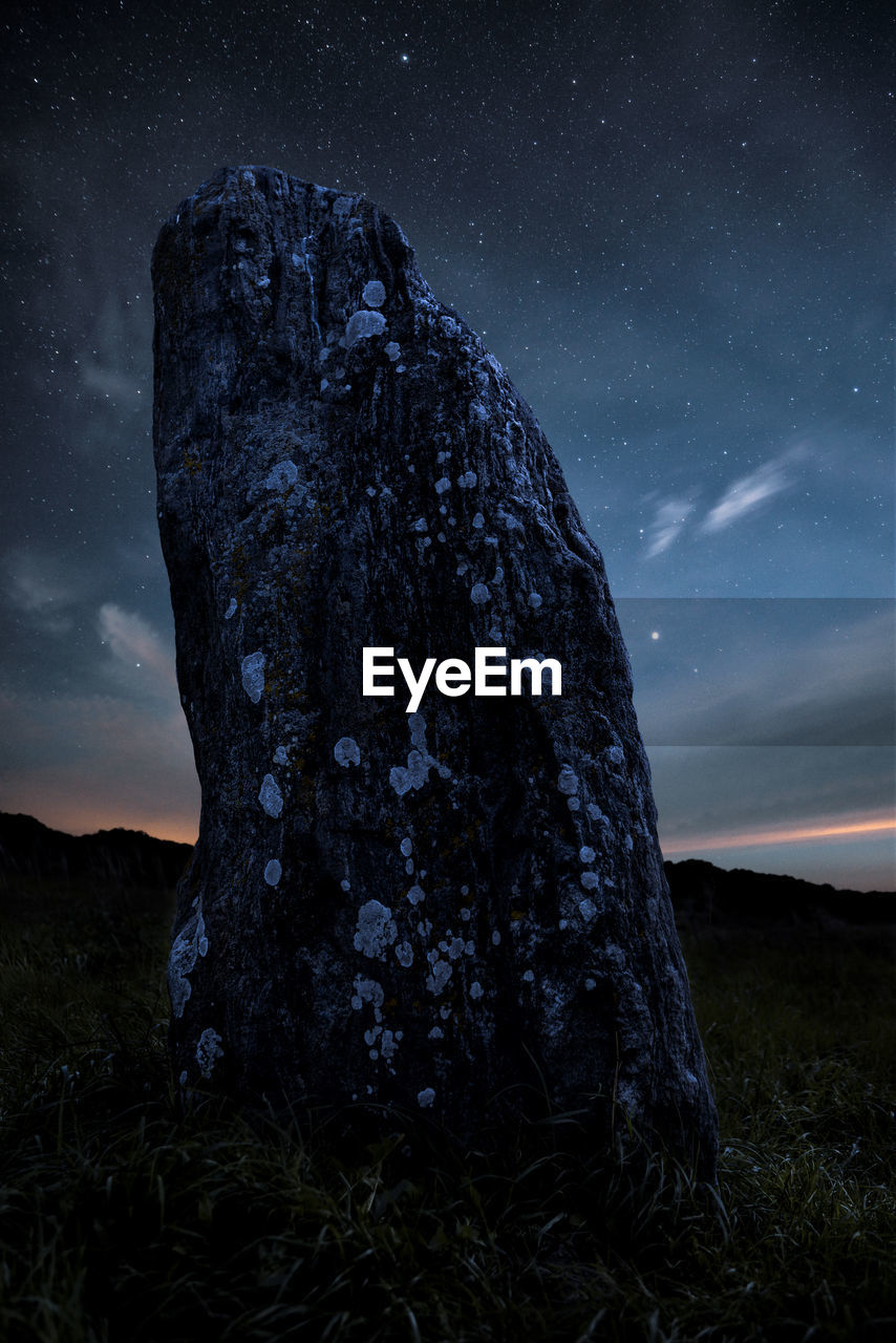 Rock formation on field against sky at night