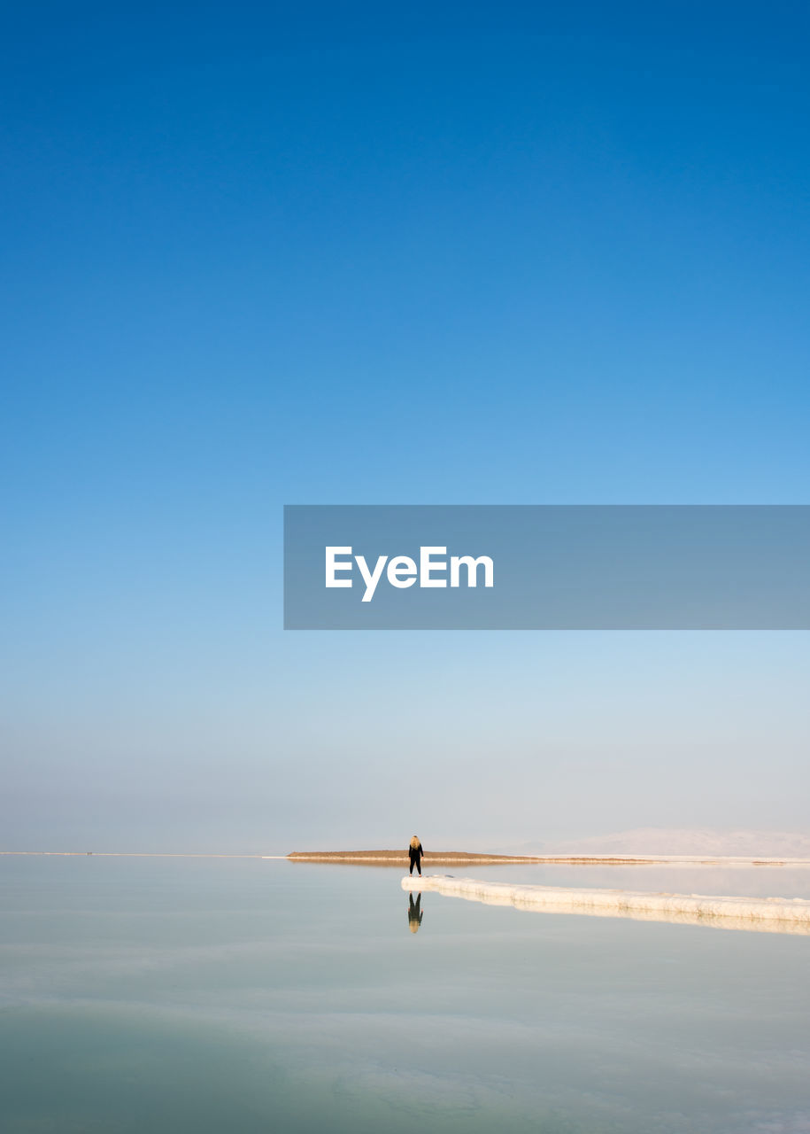 Person standing on beach against clear blue sky