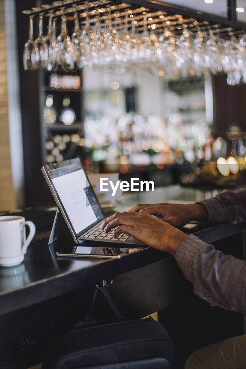 Hands of businessman typing on laptop at bar counter in restaurant