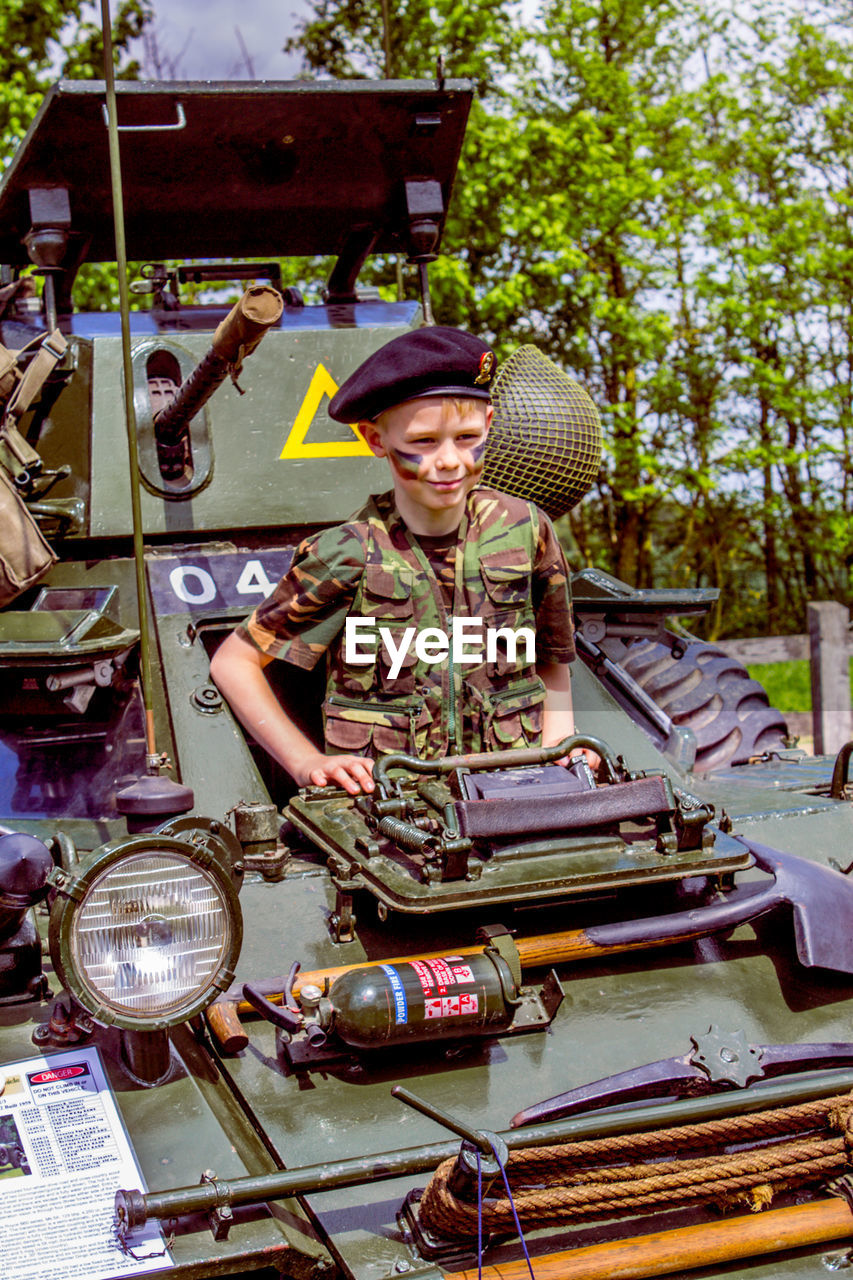 Boy wearing camouflage while standing in armored tank