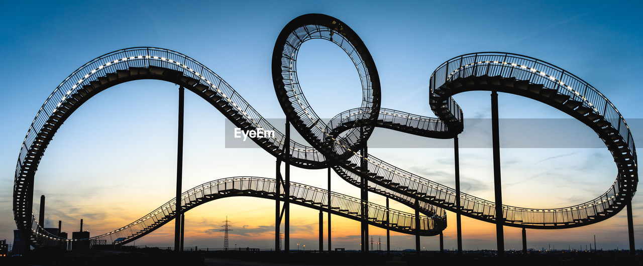 Low angle view of illuminated rollercoaster against sky during sunset