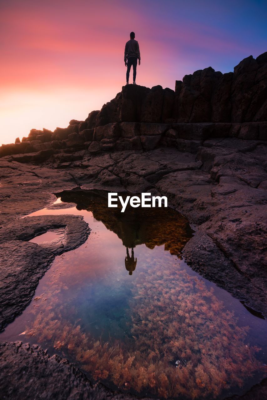 Silhouette man on rock reflecting in water man at sunset