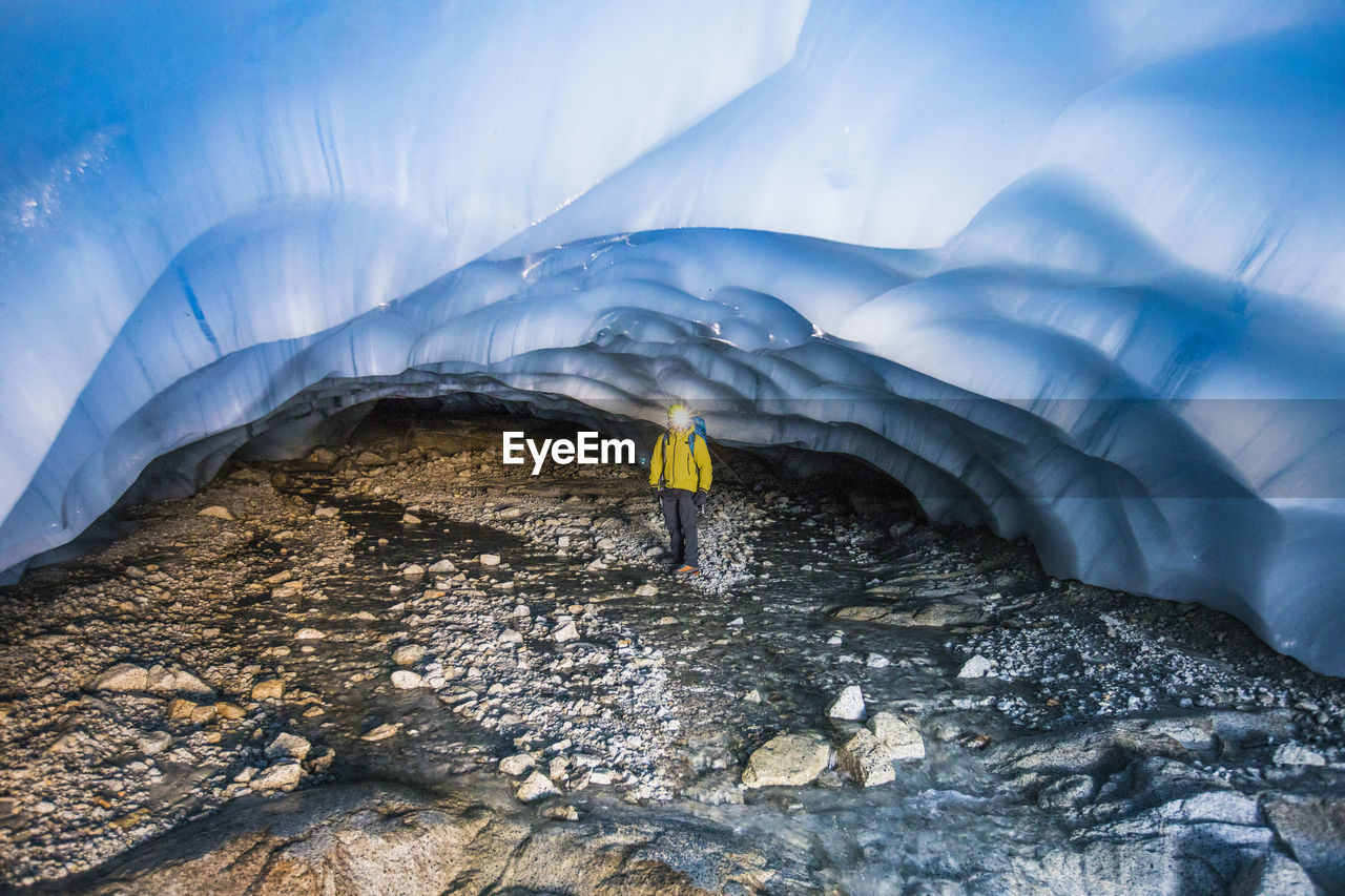 Explorer standing under glacier in cave.