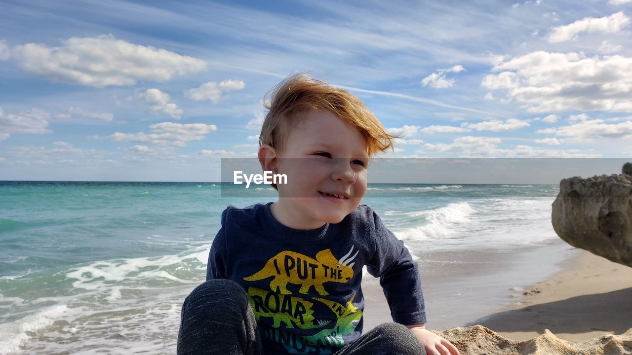 Smiling boy sitting at beach against sky