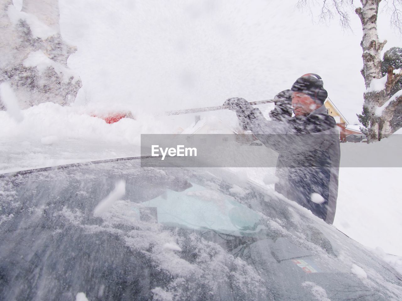 Senior man removing snow from car roof during winter