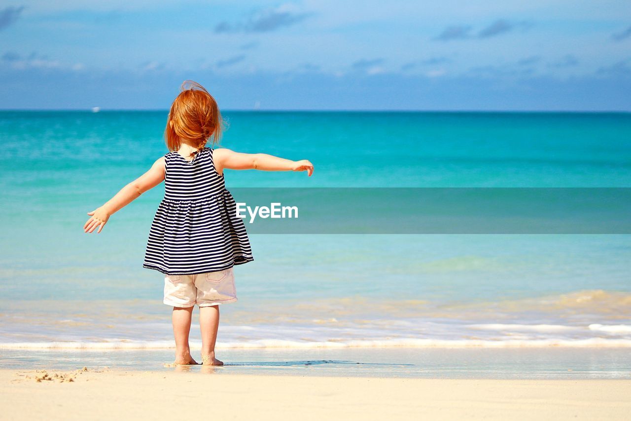 Rear view of girl standing on beach against sea